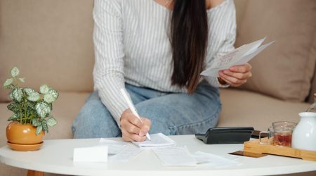 Cropped image of young woman doing home bookkeeping, checking bills and writing in notebook